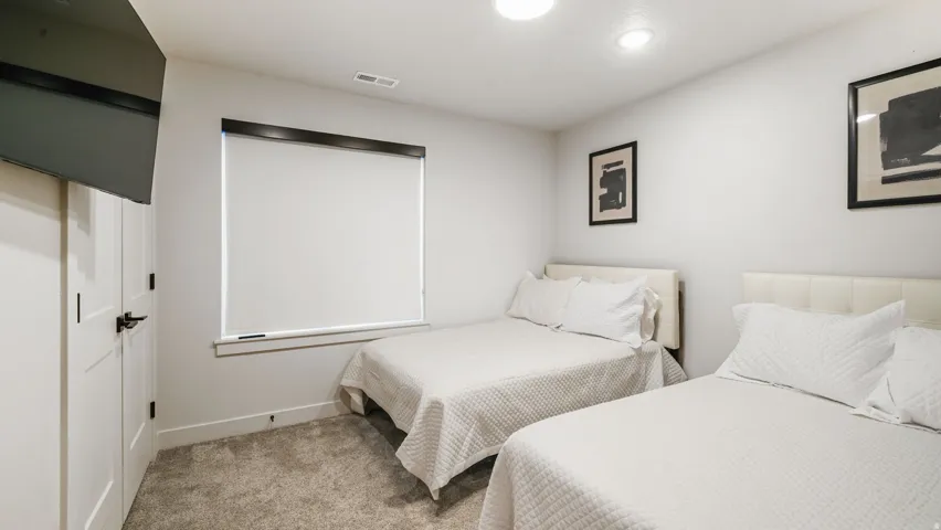 Bedroom featuring neutral wall colors, recessed lighting, wall-mounted television, and a window with a roller shade