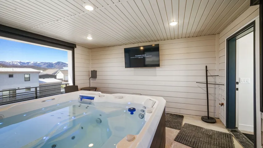 Covered outdoor patio featuring a built-in hot tub, recessed lighting, wall-mounted television, and expansive mountain scenery