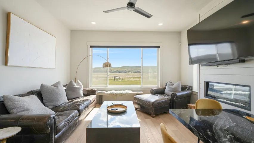 Open-concept living area featuring light wood-finish flooring, a linear electric fireplace with shiplap surround, a large picture window with a window seat, and recessed lighting