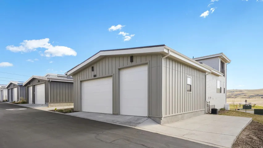 Property featuring a two-car garage with white panel doors, board and batten siding, a concrete driveway, and an additional concrete pad