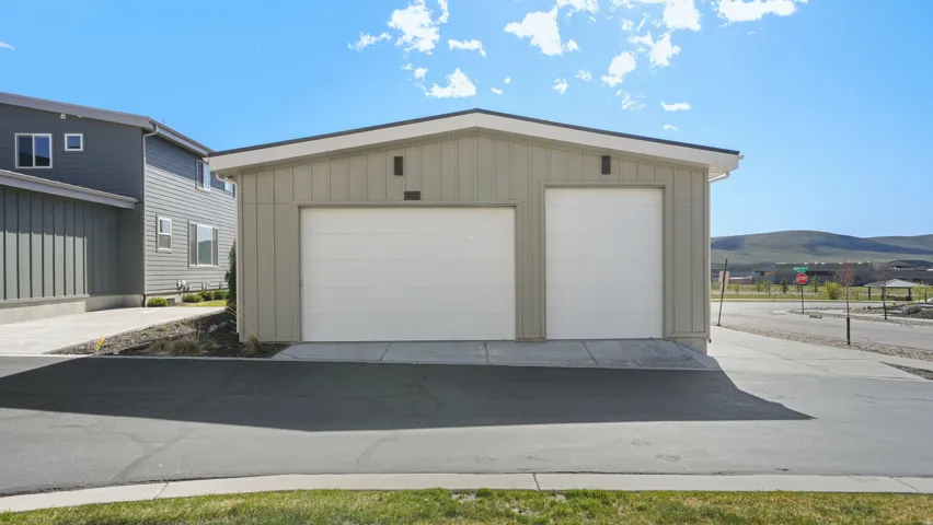 Detached two-door garage with a light tan vertical panel exterior, white garage doors, and a dark asphalt driveway