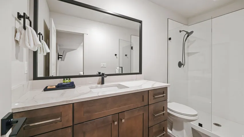 Bathroom featuring a wood-finish vanity with a white countertop, an integrated rectangular sink, a matte black faucet, and a large framed mirror