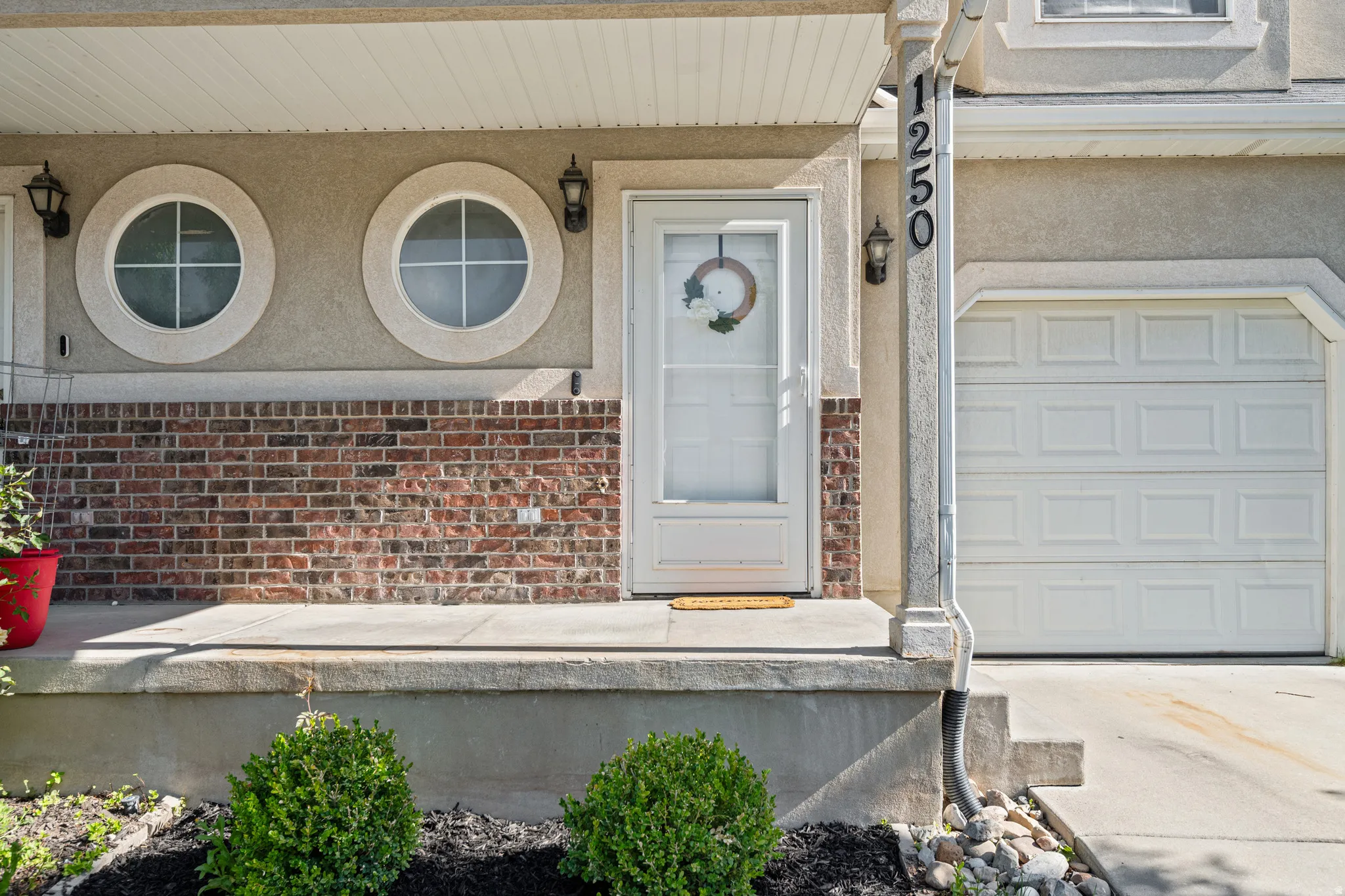 Front entrance featuring a storm door, brick and stucco exterior, two circular windows, and an attached single-car garage