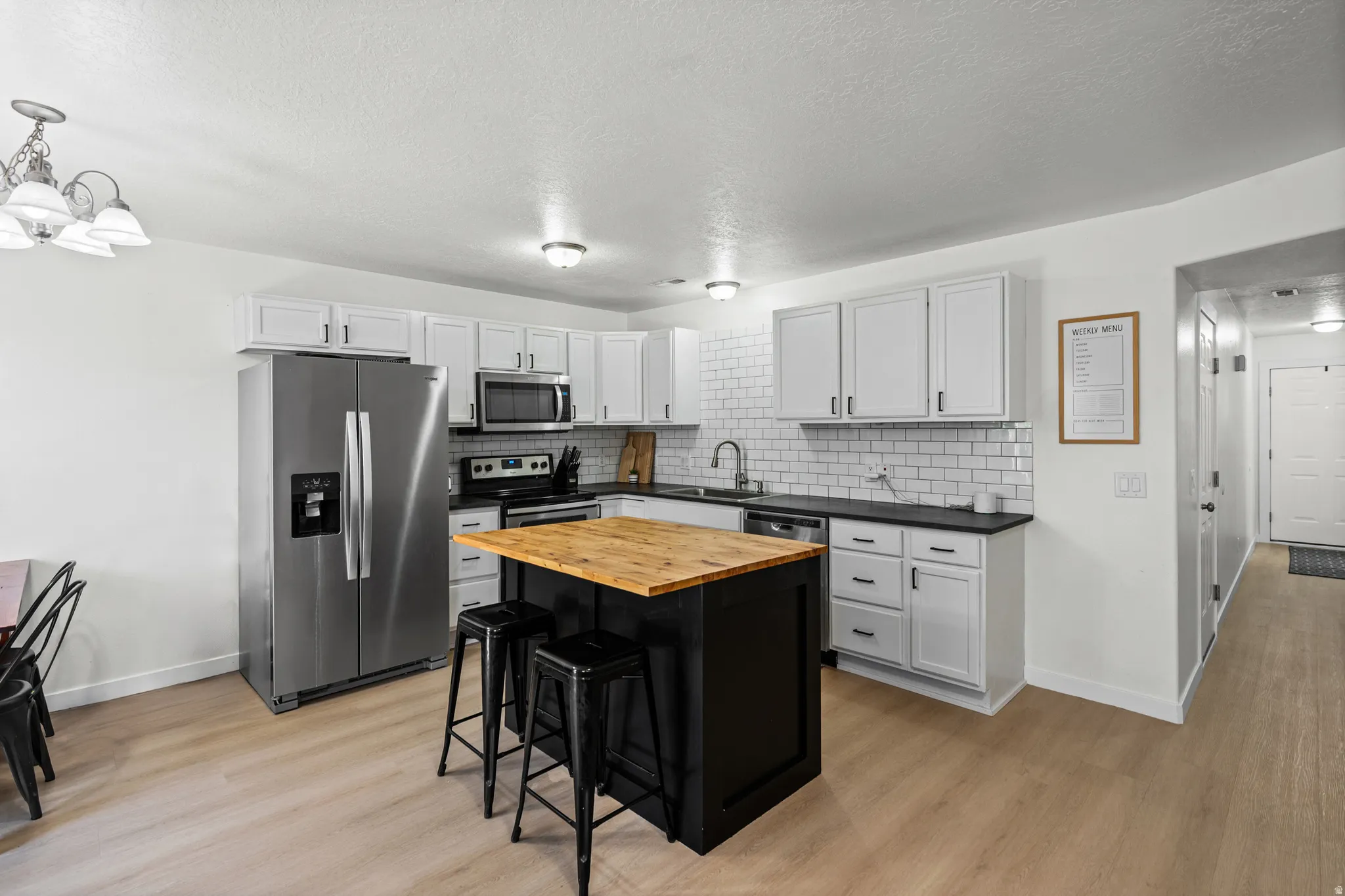 Kitchen featuring a central island with a wood-finish countertop, white cabinetry with black hardware, dark countertops, and a white subway tile backsplash