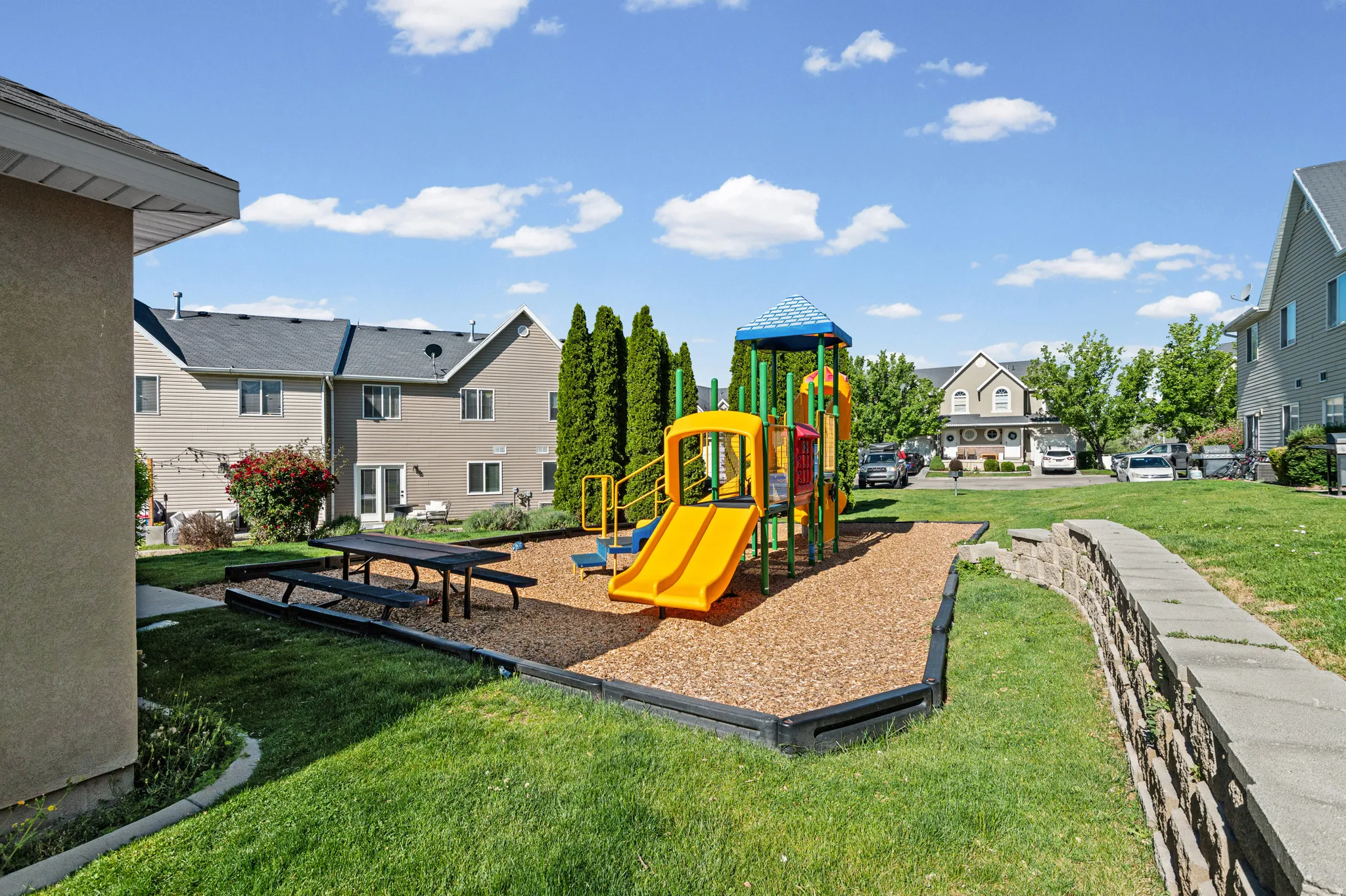 Outdoor play area featuring a multi-level play structure with slides and climbing elements, set on a wood chip surface