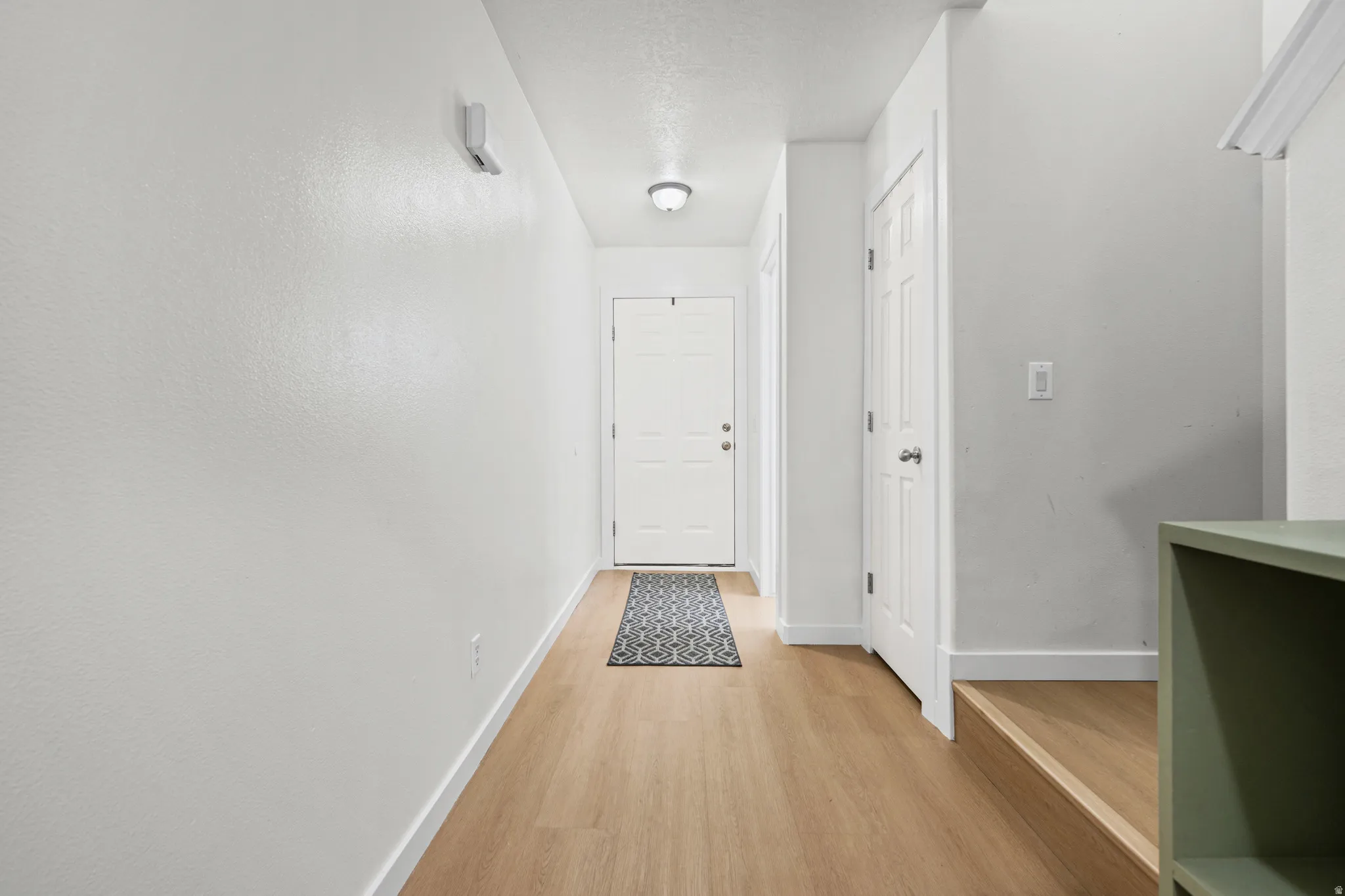 Light wood-finish flooring extends through this entryway, featuring a white paneled door, flush-mount lighting, and crisp white walls