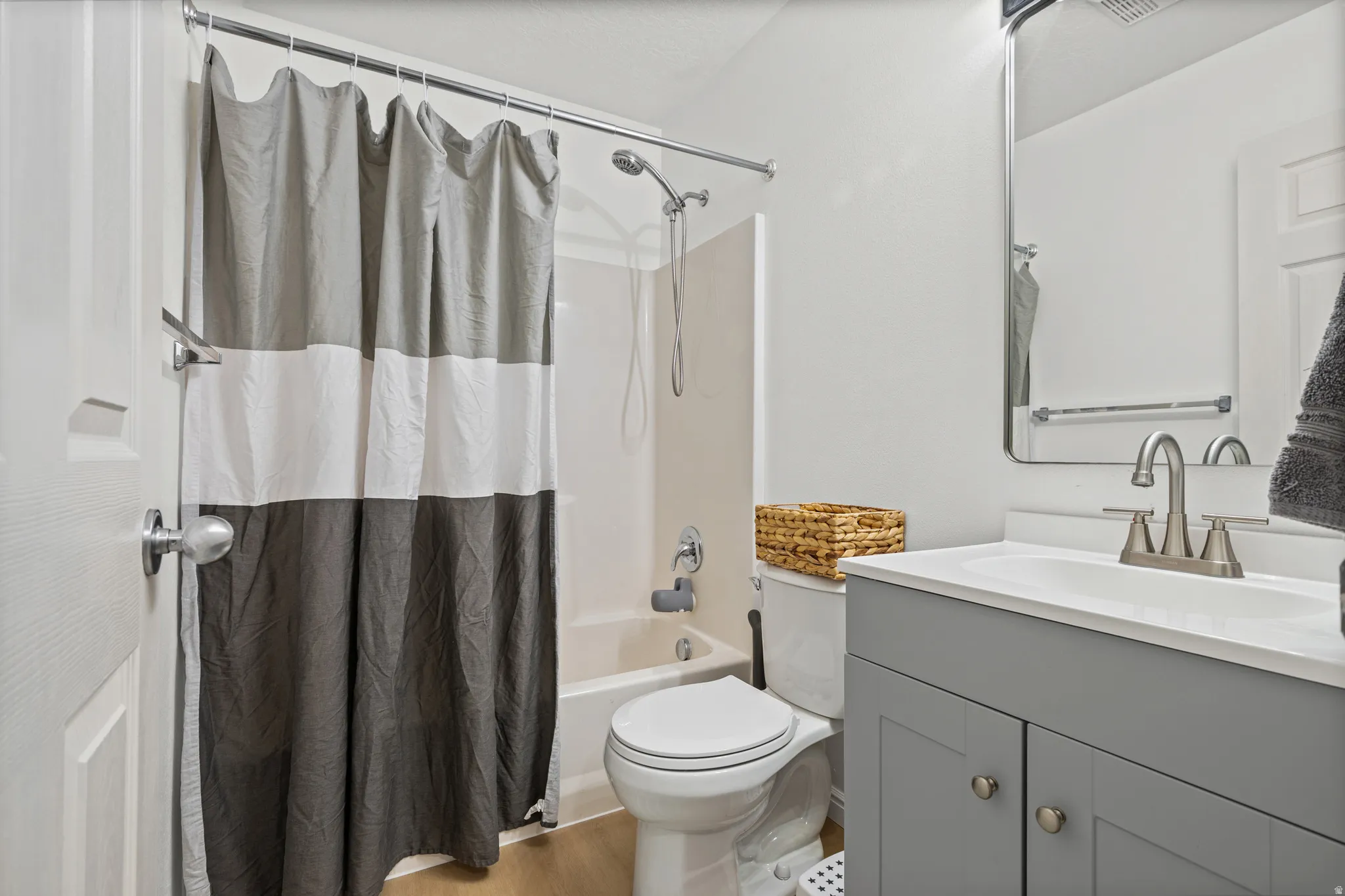 Bathroom featuring a vanity with a white countertop and gray cabinetry, brushed nickel faucet, wall-mounted mirror, and a shower/tub combination
