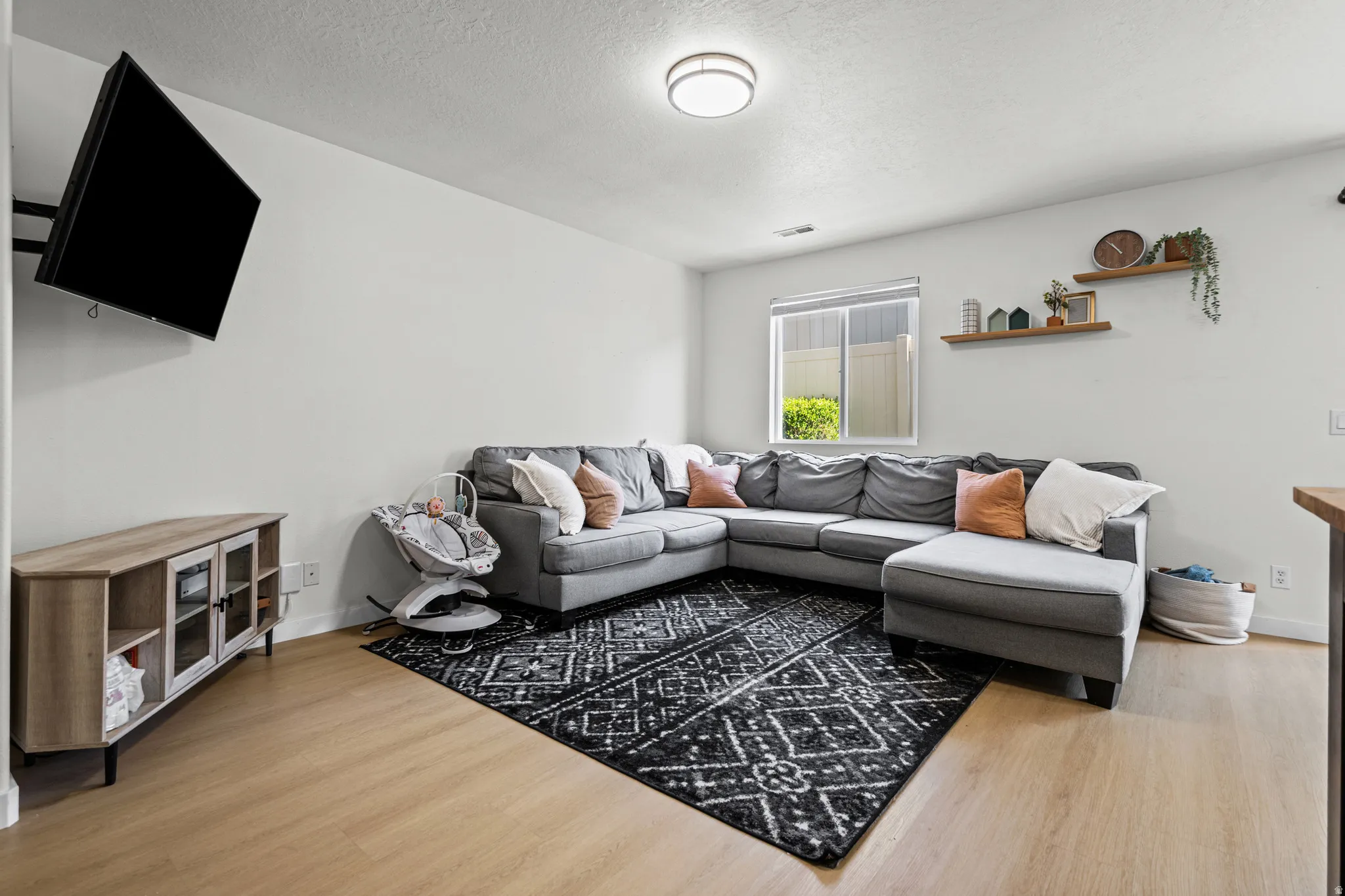 Living area featuring wood-finish flooring, light-toned walls, and a window with blinds