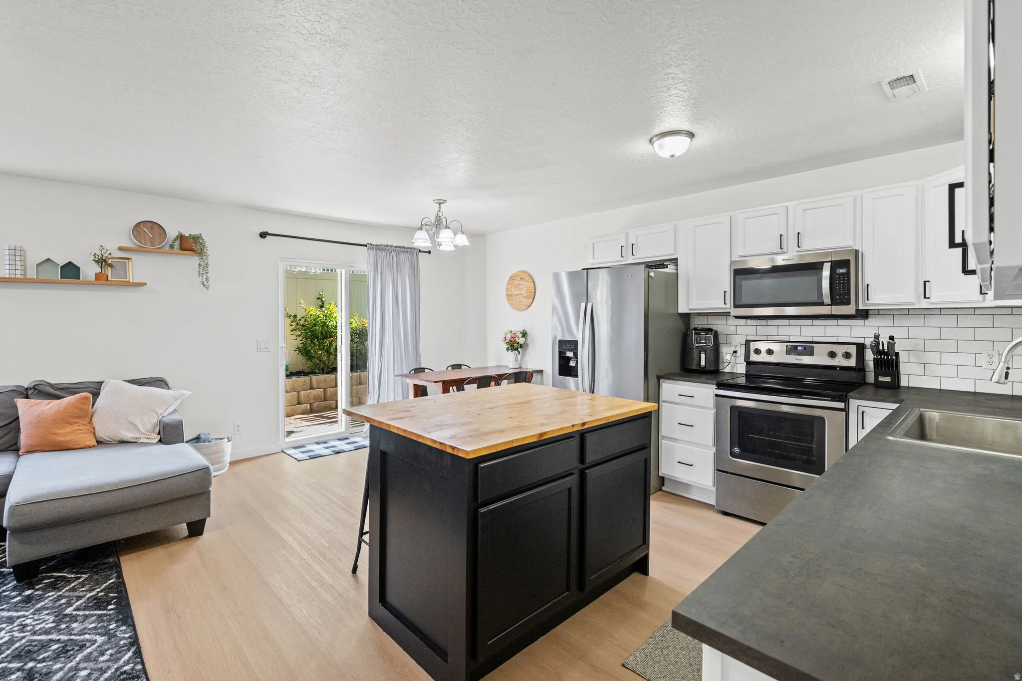 Kitchen featuring stainless steel appliances, subway tile backsplash, white cabinetry, and a black island with a wood-finish countertop