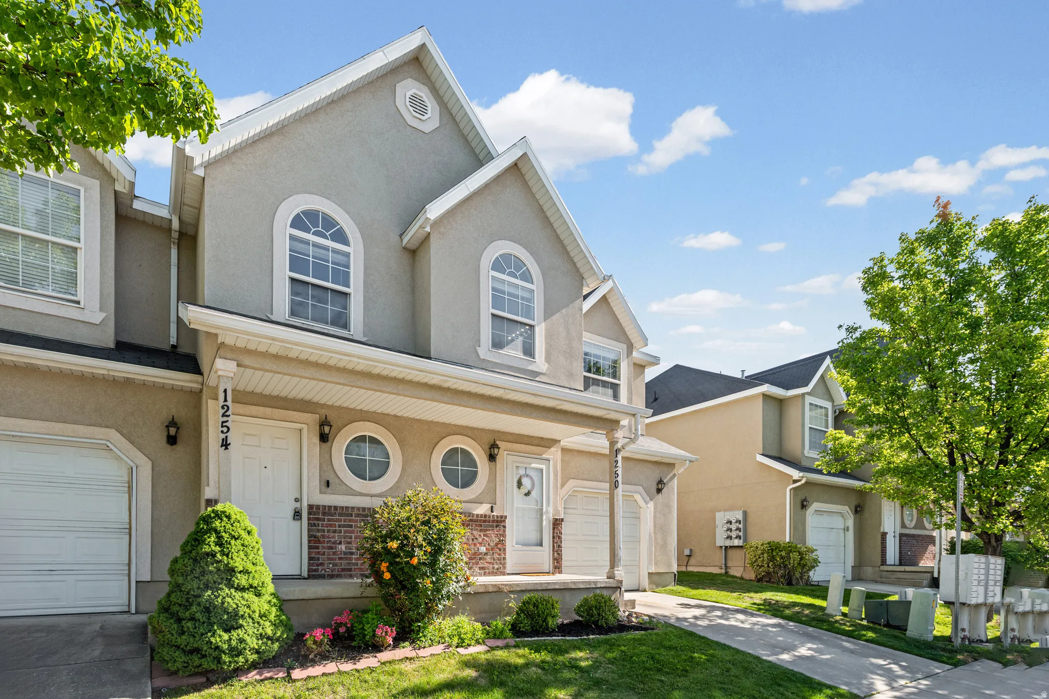 Stucco exterior featuring arched and circular windows, an attached single-car garage, brick accents, and a covered porch entry