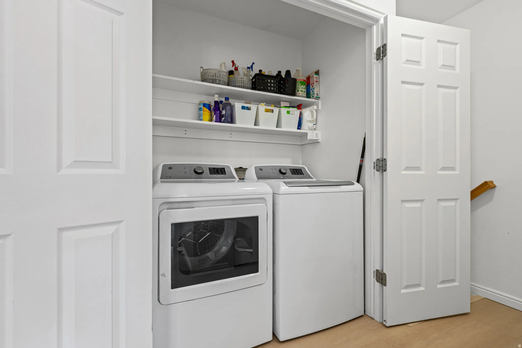 Dedicated laundry area featuring a washer and dryer set, two wall-mounted shelves, white paneled doors, and light-toned flooring