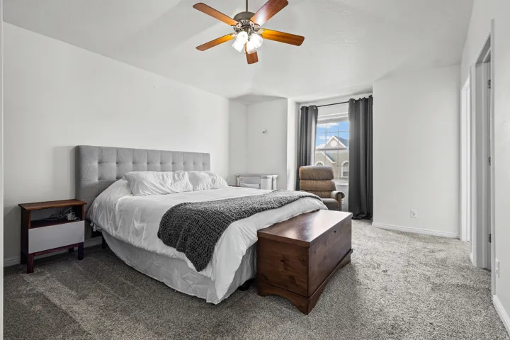 Spacious room featuring neutral carpeting, light-colored walls, a ceiling fan with light fixture, and a window with dark drapery