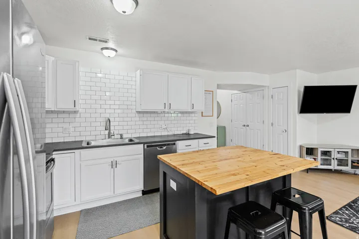 Contemporary kitchen featuring white shaker cabinetry, dark countertops, subway tile backsplash, stainless steel appliances, and a butcher block island