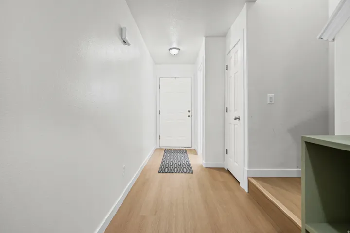 Light wood-finish flooring extends through this entryway, featuring a white paneled door, flush-mount lighting, and crisp white walls