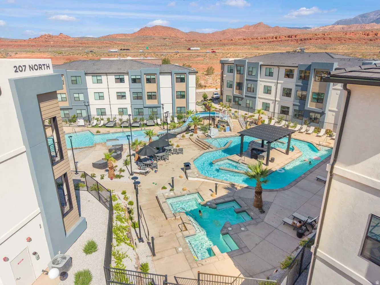 Resort-style pool area featuring multiple swimming zones, a covered pergola, integrated hot tubs, and surrounding lounge areas