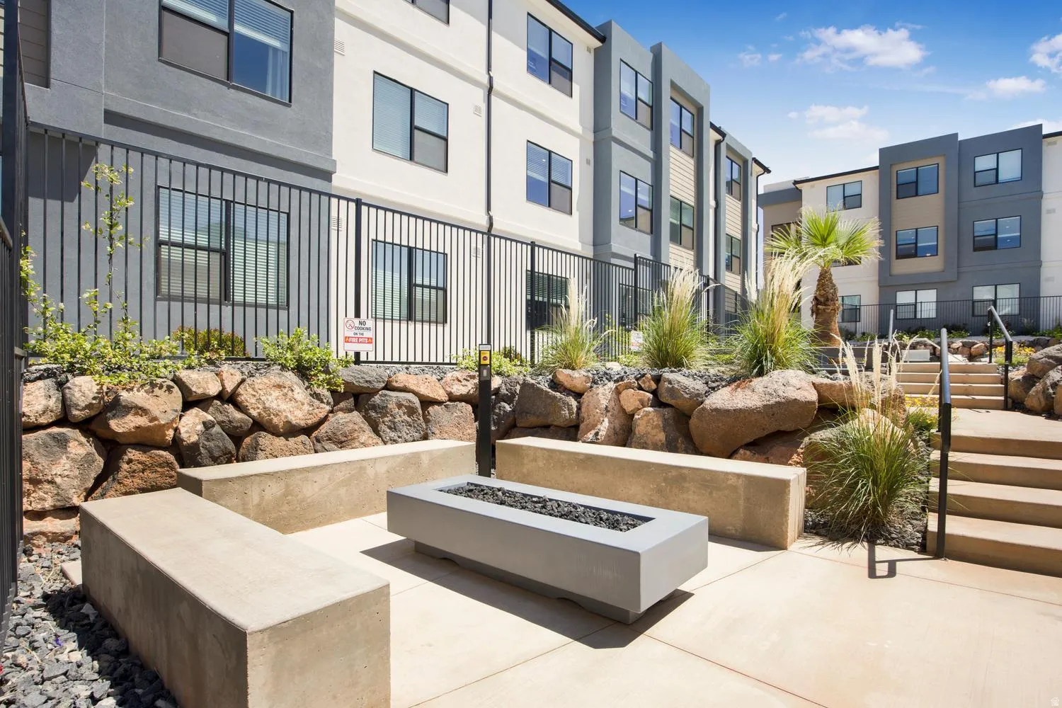 Outdoor patio featuring a rectangular fire pit, built-in concrete benches, and a rock retaining wall with natural landscaping