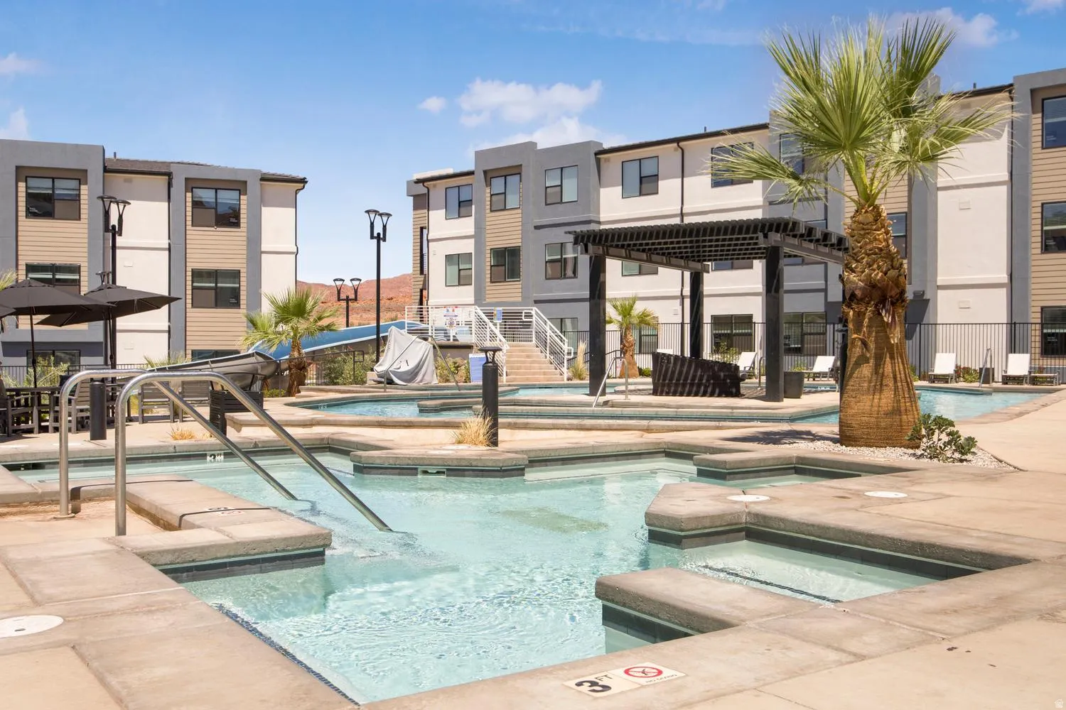 Multi-level pool area featuring integrated spas, a shaded pergola, and surrounding lounge seating