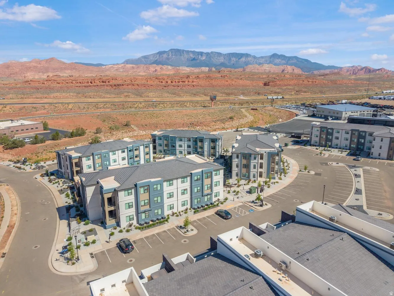 Modern apartment buildings with a neutral and blue facade, surrounded by structured parking areas and landscaping