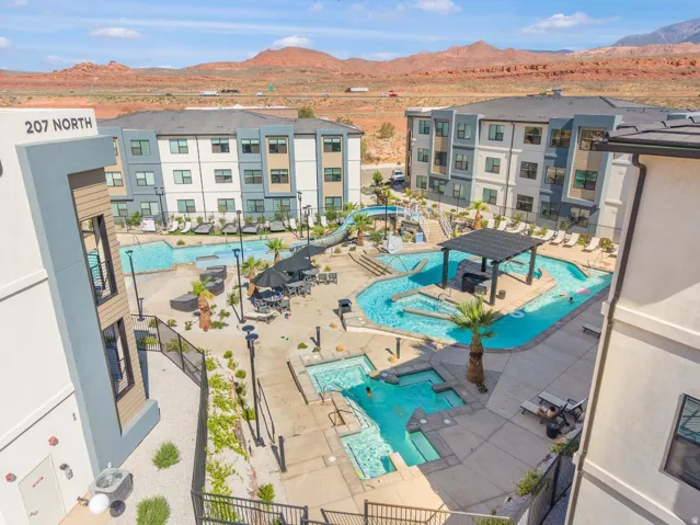 Resort-style pool area featuring multiple swimming zones, a covered pergola, integrated hot tubs, and surrounding lounge areas