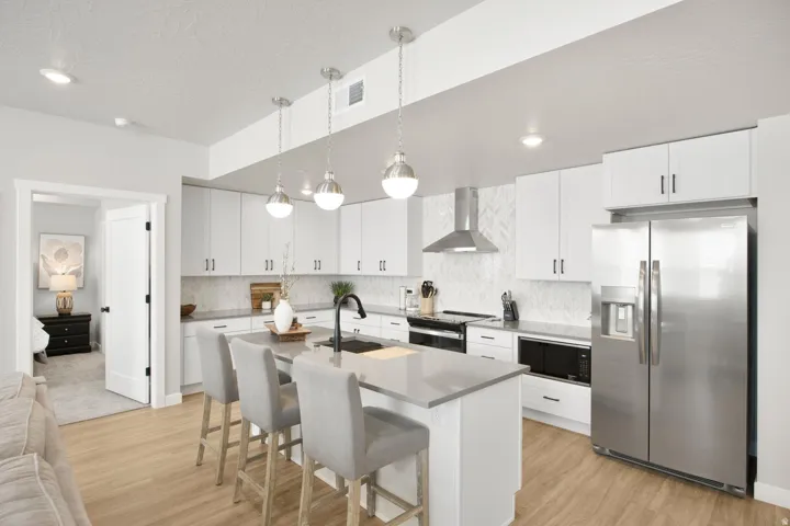 Open-concept kitchen featuring an island with seating, white shaker cabinetry, stainless steel appliances, and wood-finish flooring