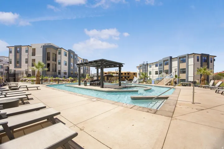 Resort-style pool area featuring a custom pool, integrated lounging areas, and a shaded pergola