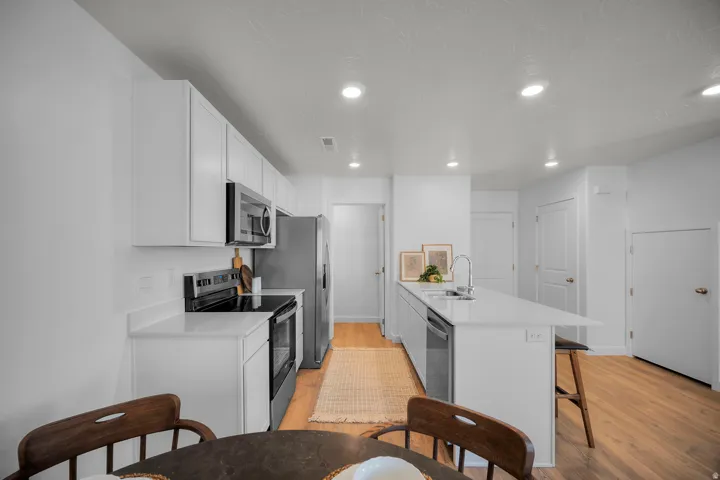Open-concept kitchen featuring white cabinetry, stainless steel appliances, white countertops, and wood-finish flooring