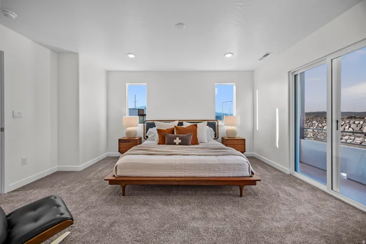 Spacious bedroom featuring neutral carpeting, recessed lighting, two vertical windows, and a sliding glass door providing outdoor access