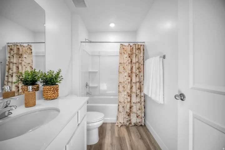 Contemporary bathroom featuring a single vanity with a white countertop and integrated sink, chrome faucet, and wood-finish flooring
