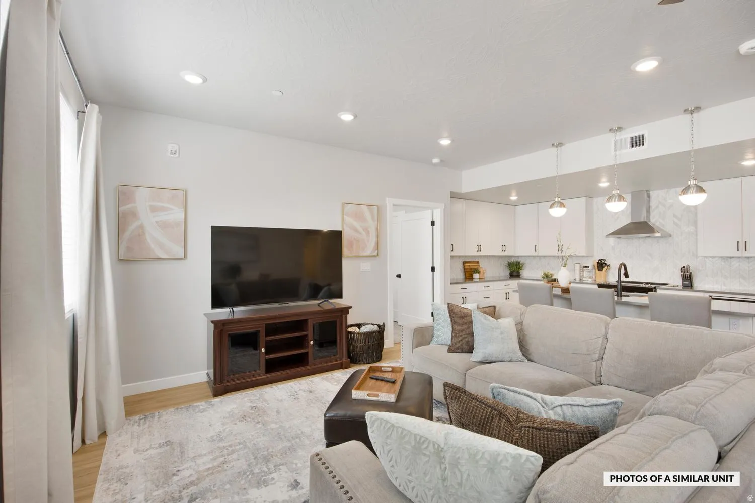 Open-concept living space featuring recessed lighting, wood-finish flooring, and a kitchen with white cabinetry, a herringbone tile backsplash, and pendant lighting