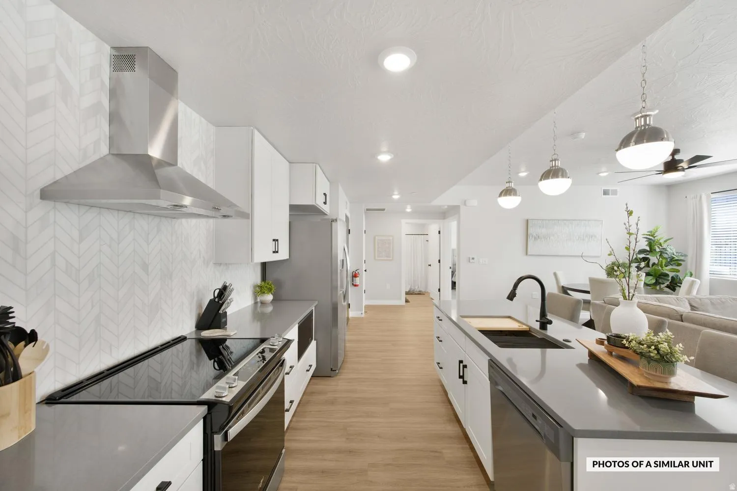 Modern kitchen featuring a chevron-patterned backsplash, stainless steel range hood, sleek black appliances, white cabinetry with dark hardware, and a center island with a black sink and matte black faucet