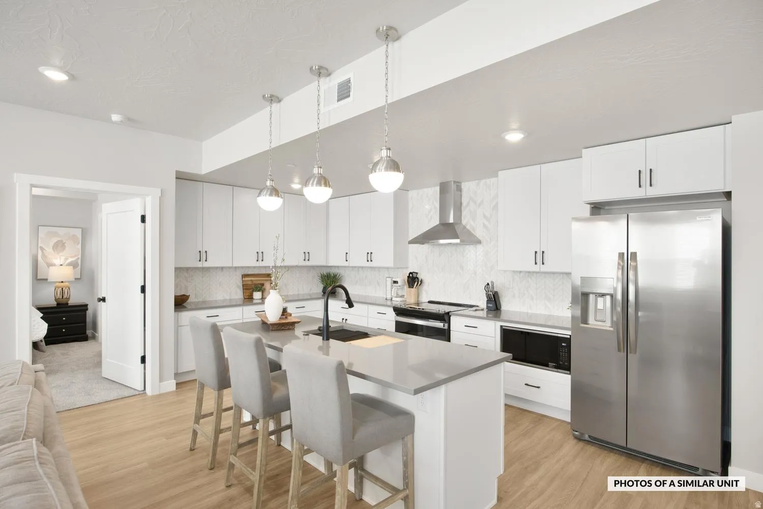 Open-concept kitchen featuring an eat-at island, stainless steel appliances, white cabinetry, and wood-finish flooring