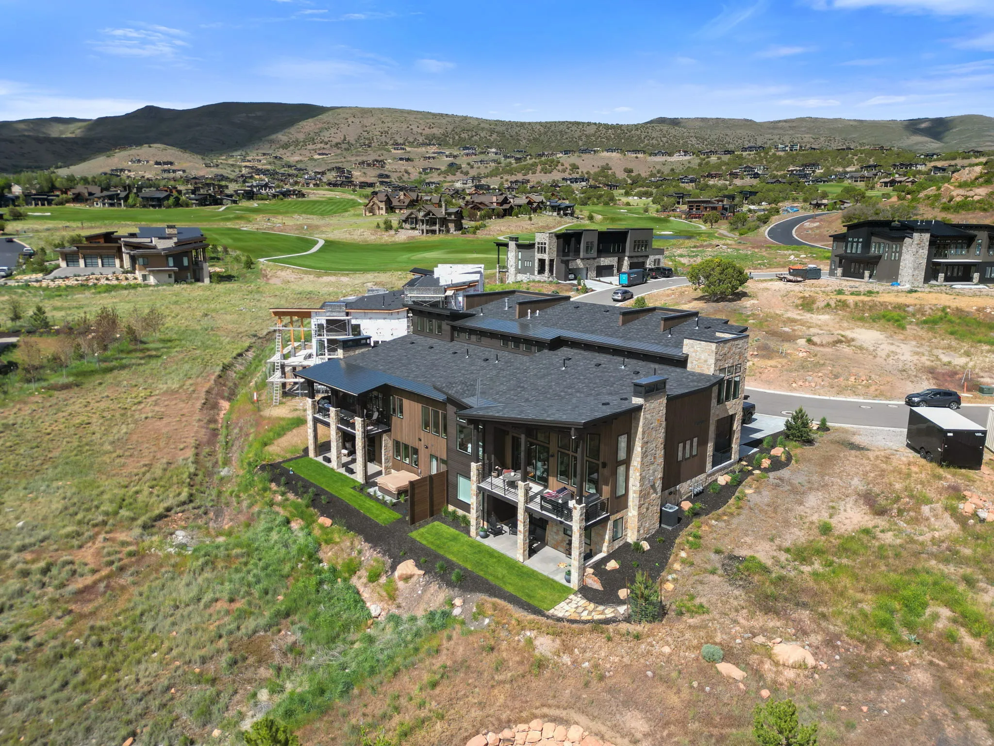 Modern multi-story residence featuring a dark shingle roof, stone and wood-panel exterior, multiple balconies, and a manicured lawn
