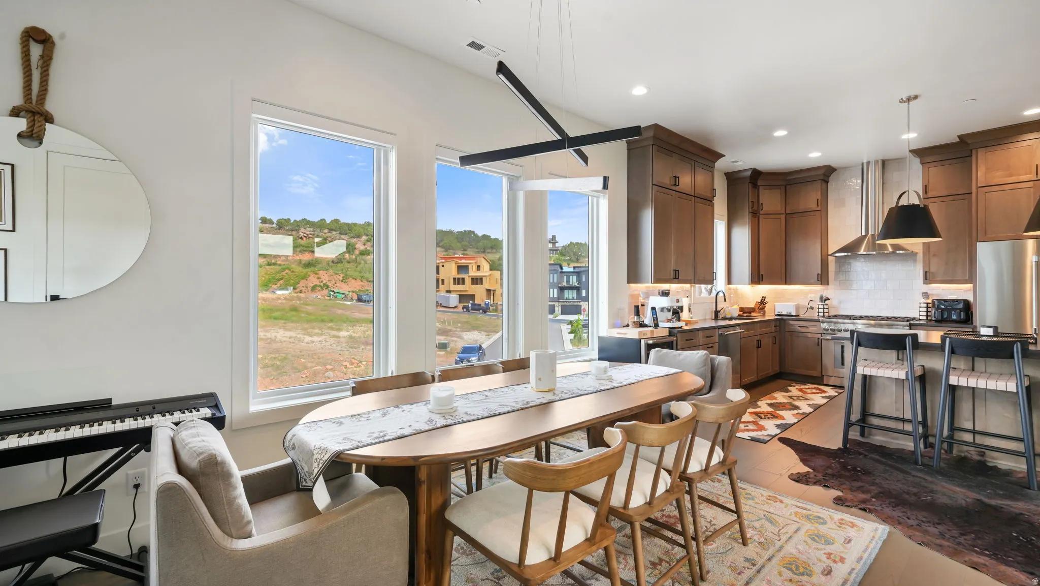 Open-concept living space with large windows, a dining area, and a kitchen featuring dark wood cabinetry, stainless steel appliances, and a tiled backsplash