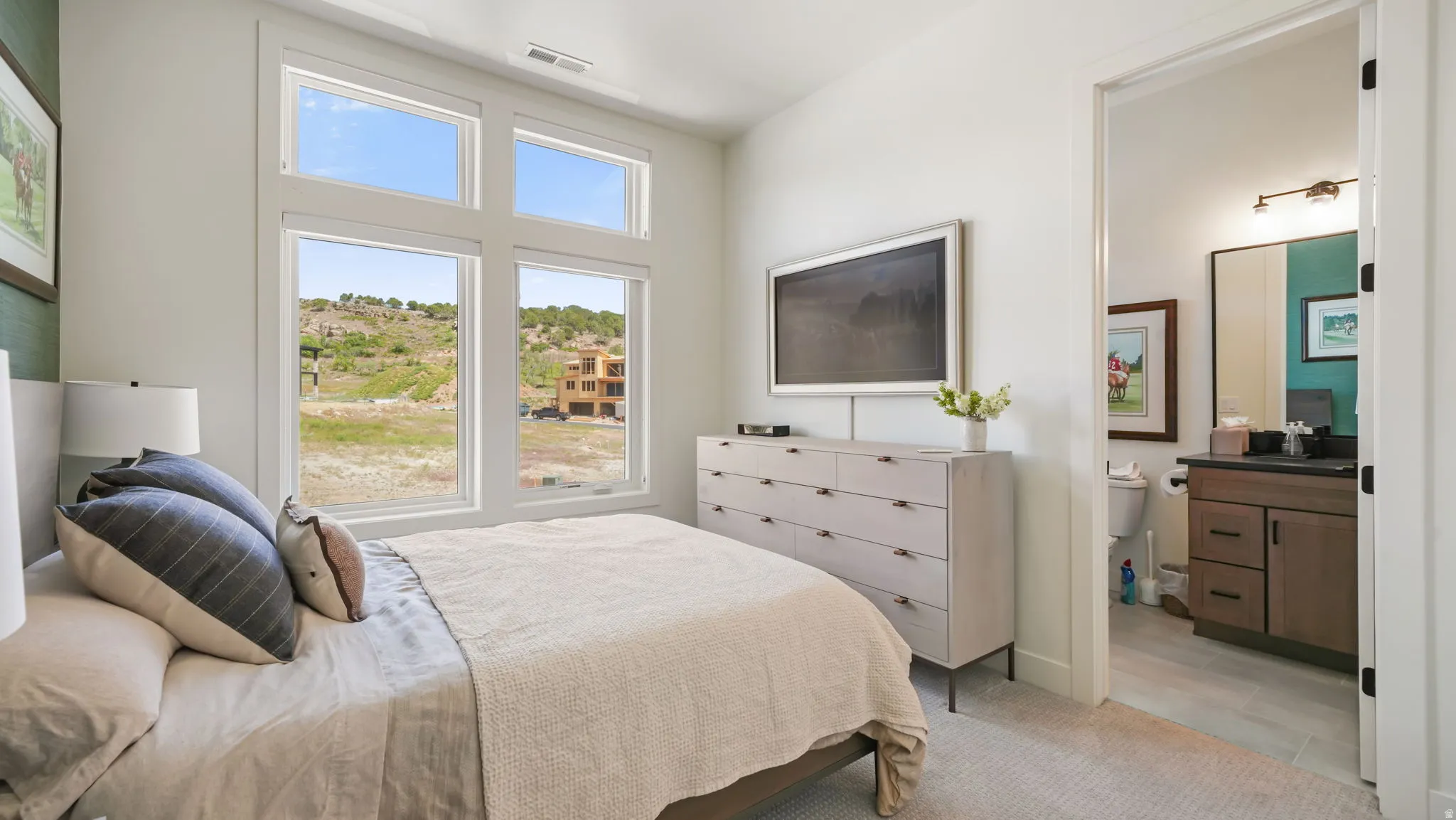 Spacious room featuring multiple large windows, ample natural light, soft carpet flooring, and an en-suite bathroom with a vanity and mirror