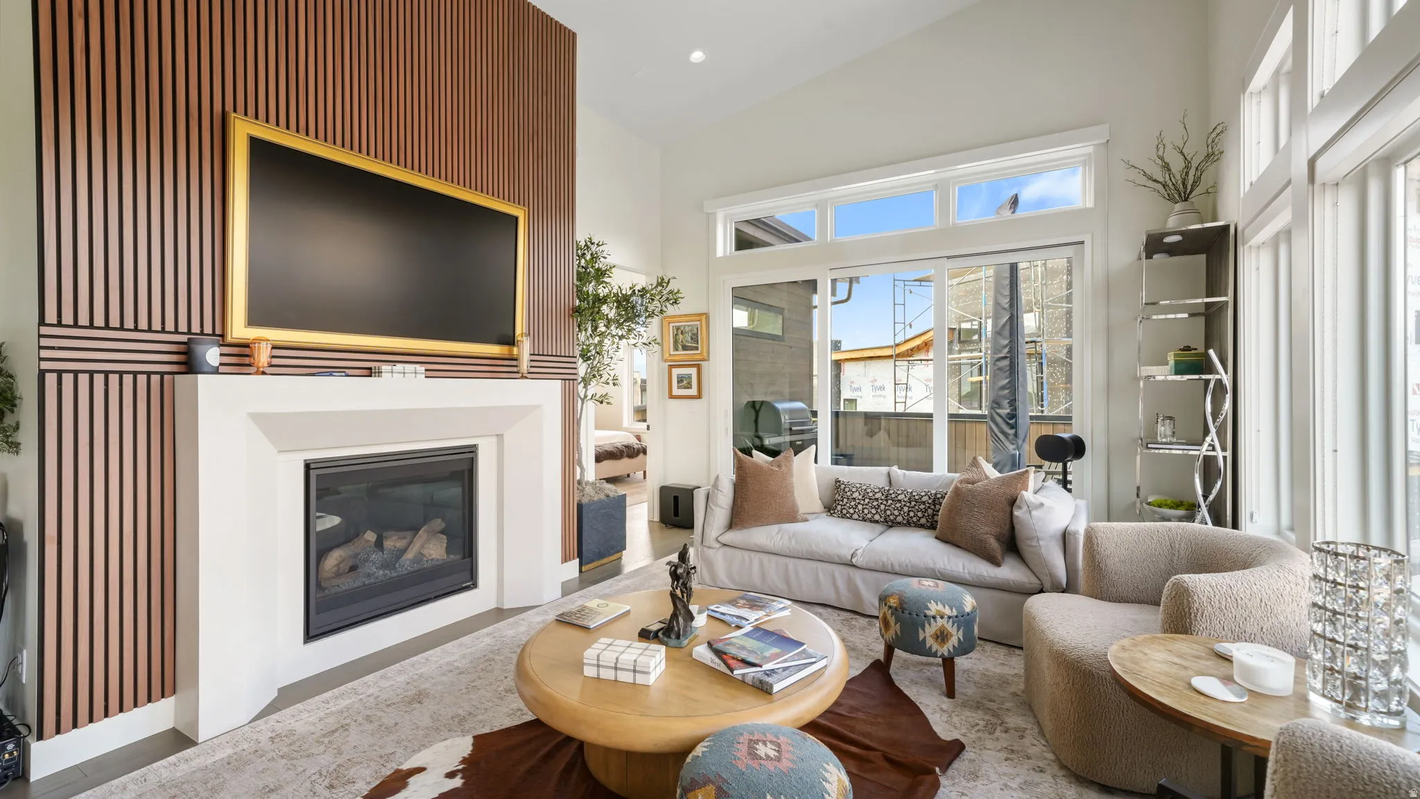 Vaulted ceiling living area featuring a fireplace with a stone surround, a wood-slat accent wall, and expansive glass sliding doors
