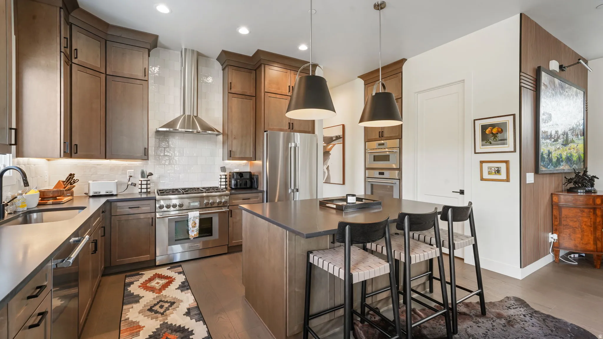 Modern kitchen featuring wood-finish cabinetry, stainless steel appliances, a center island with pendant lighting, a tile backsplash, and wood-finish flooring