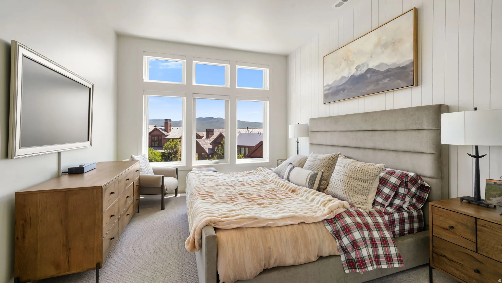 Bright bedroom with multiple windows, featuring a paneled accent wall and a built-in window seat