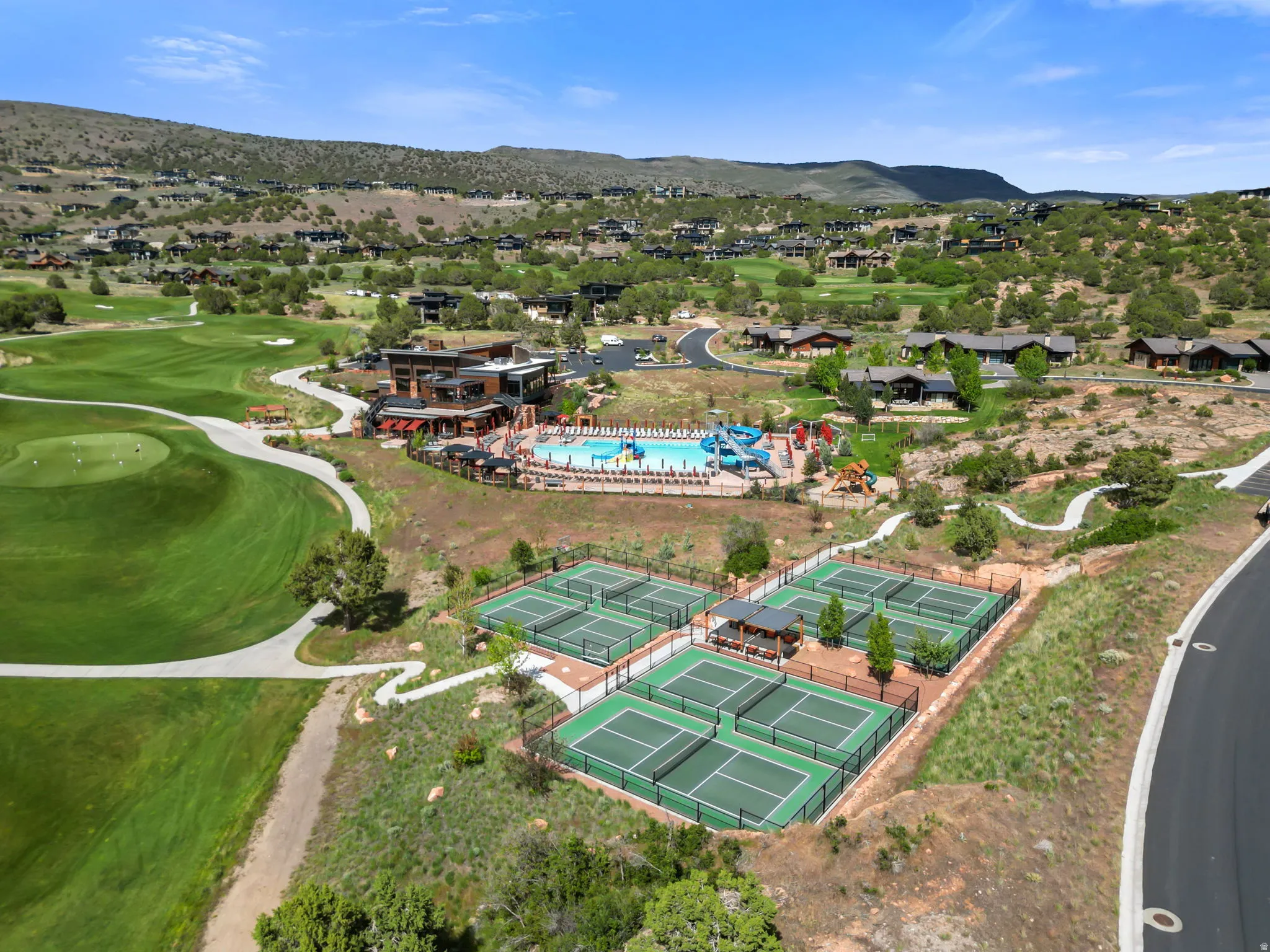 Expansive property featuring golf course greens, multiple tennis courts, a large swimming pool complex, and surrounding residences