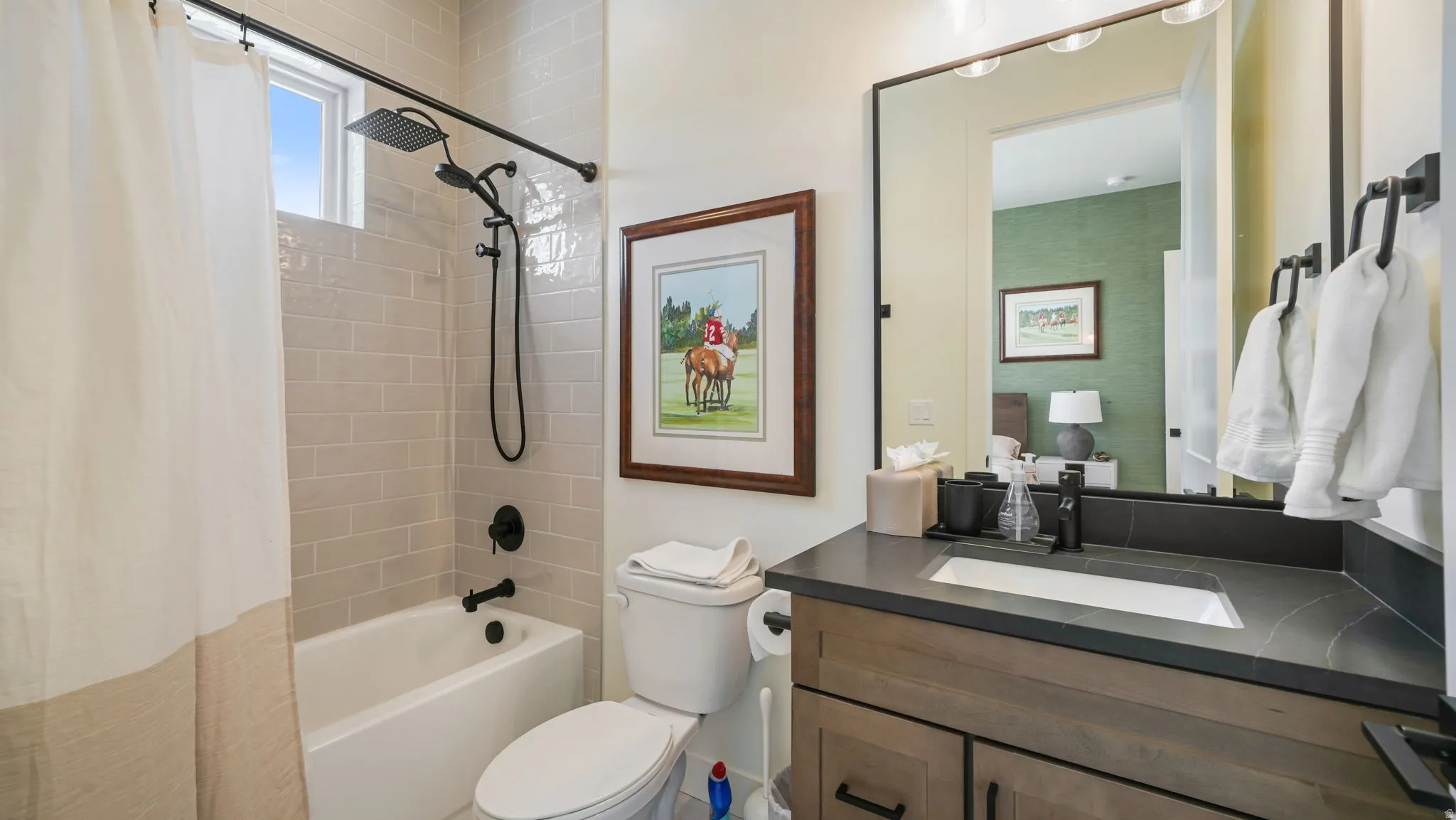 Modern bathroom featuring a soaking tub with subway tile surround, a shower system with a rain shower head and handheld sprayer, a vanity with a dark countertop and undermount sink, and black fixtures