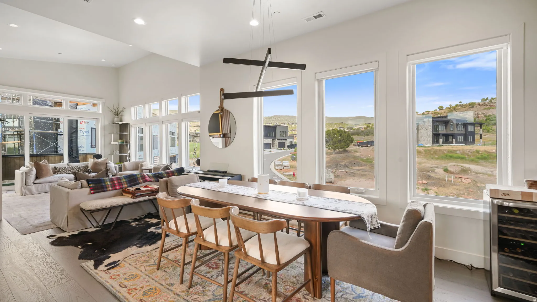 Open-concept living area featuring high vaulted ceilings, expansive windows, light wood-finish flooring, and a contemporary dining fixture