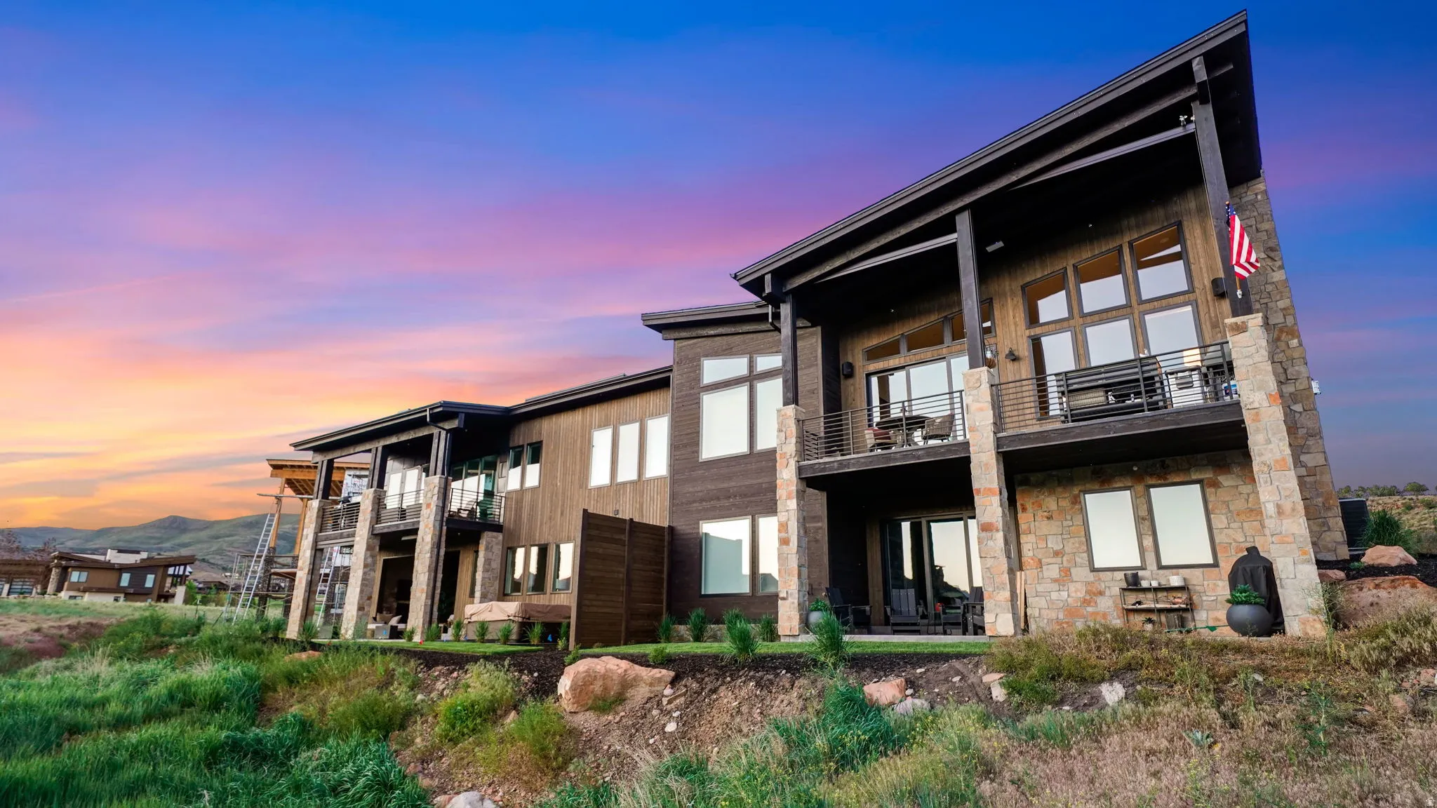 Contemporary residence featuring multi-level balconies, expansive windows, stone veneer accents, wood-finish siding, and a sloped roofline