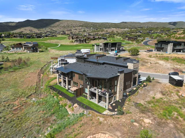 Modern multi-level residence featuring stone and wood-finish siding, multiple balconies, a dark shingle roof, and terraced landscaping