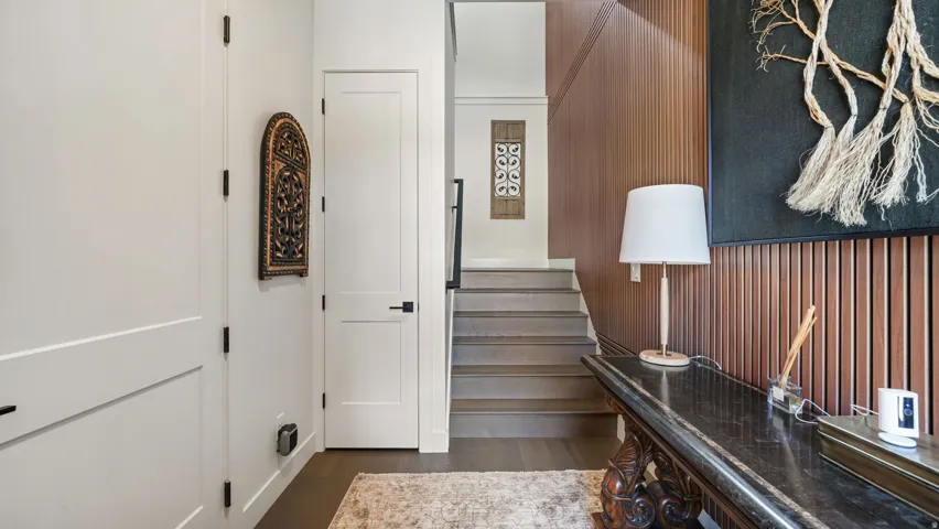 Entryway featuring a wood-panel accent wall, dark wood-finish flooring, a contemporary staircase with dark railings, and a built-in console table with a dark stone-finish surface