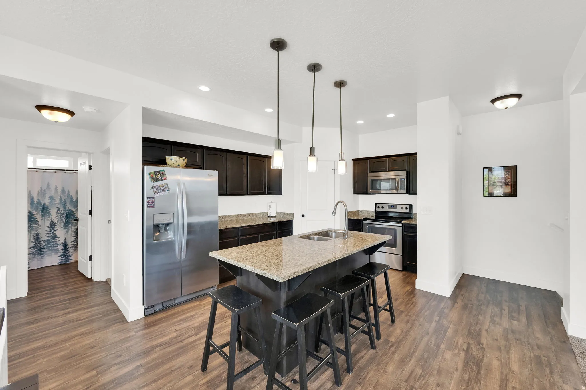 Kitchen featuring an island with stone-finish countertop and undermount sink, dark wood cabinetry, and stainless steel appliances