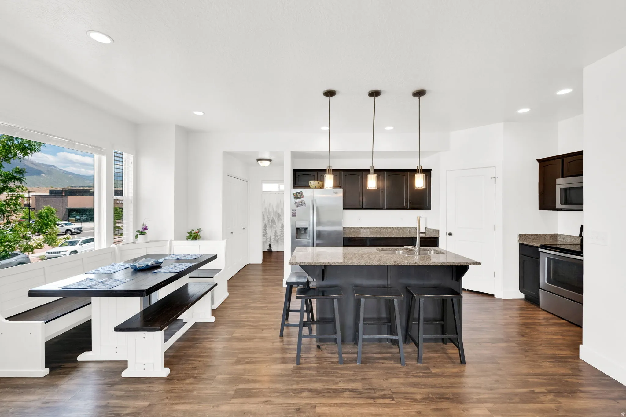 Open-concept kitchen and dining area featuring wood-finish flooring, recessed lighting, and a large window overlooking a mountain backdrop