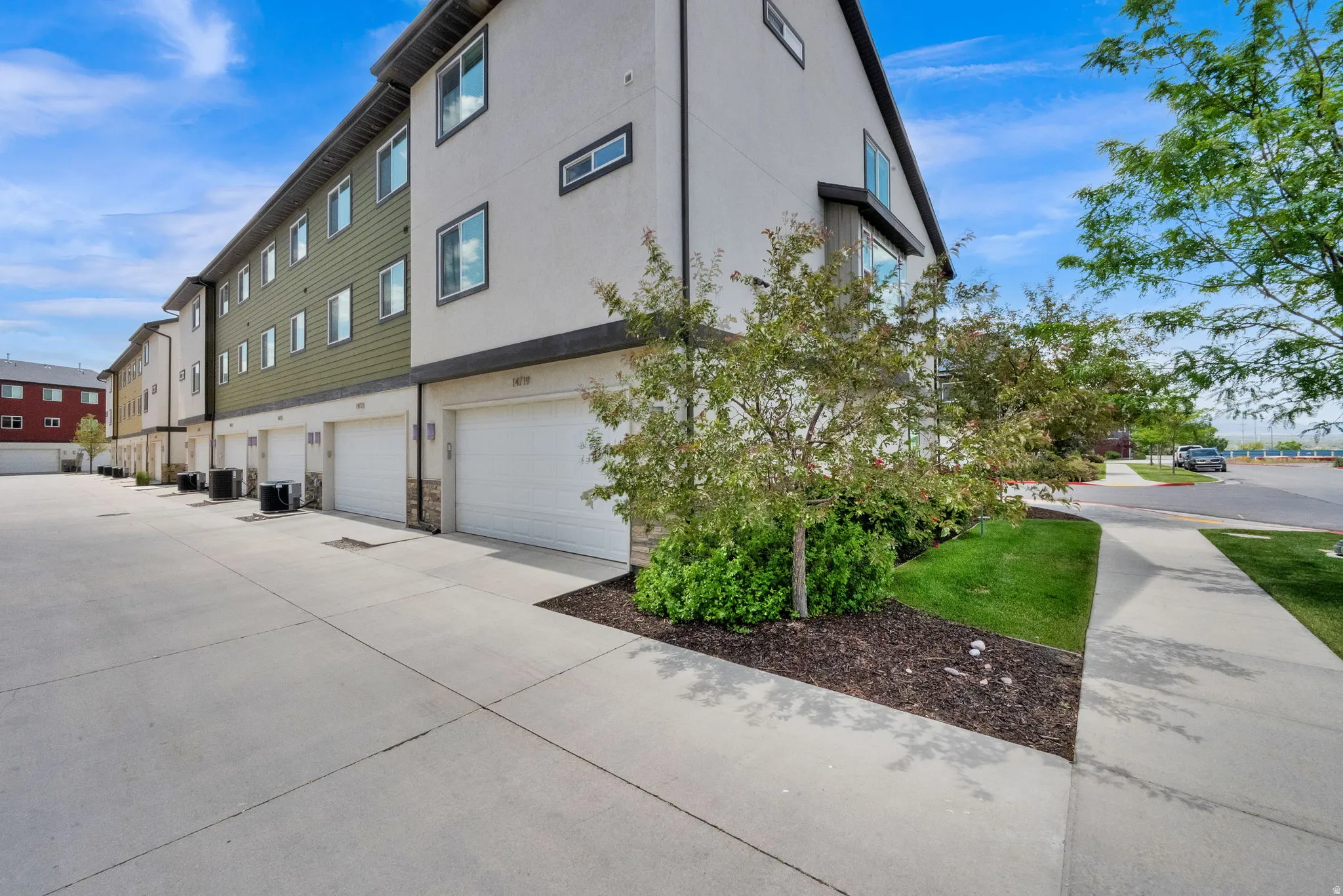 Modern townhome exterior with multiple garage bays, contemporary siding, large windows, landscaped grounds, and concrete driveways