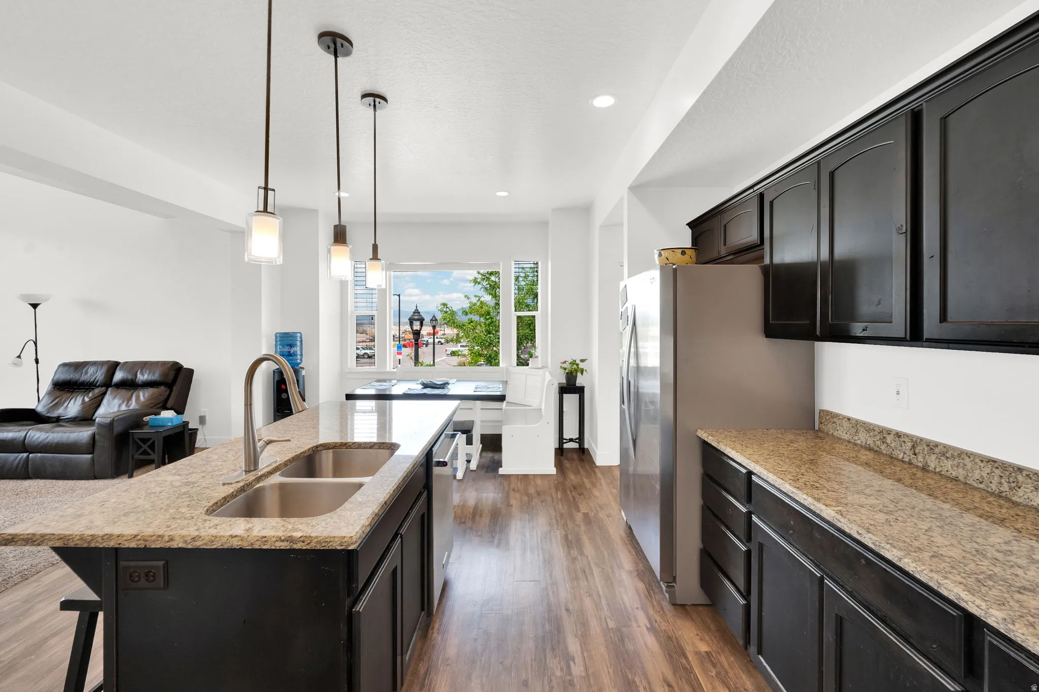 Open-concept kitchen featuring dark cabinetry, speckled countertops, and wood-finish flooring
