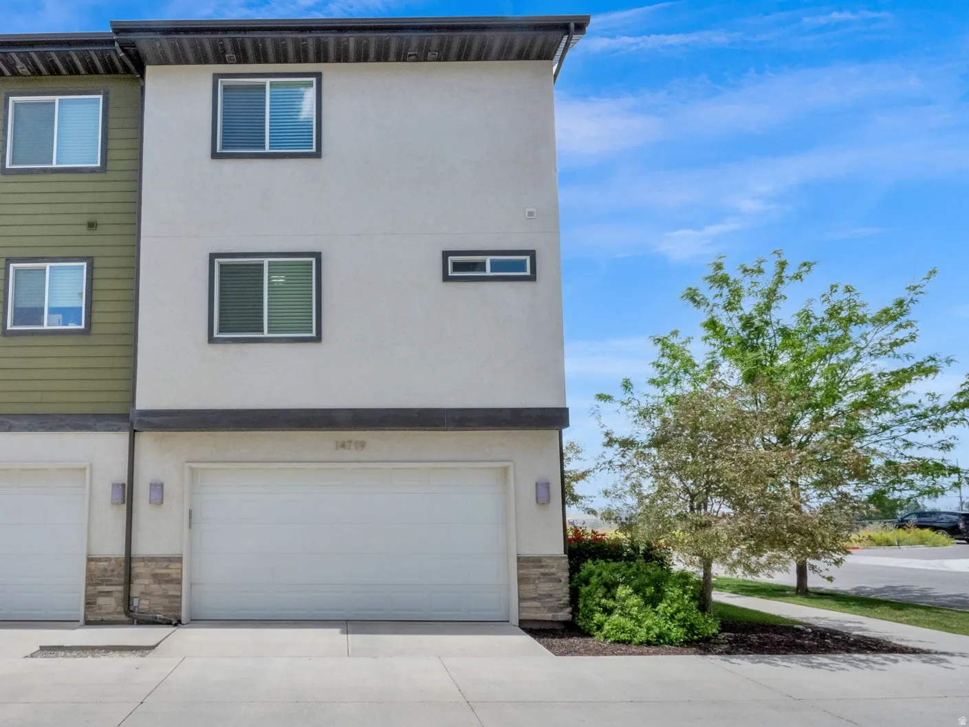 Modern multi-level exterior with a two-car garage, stucco and horizontal siding finishes, and stone veneer accents