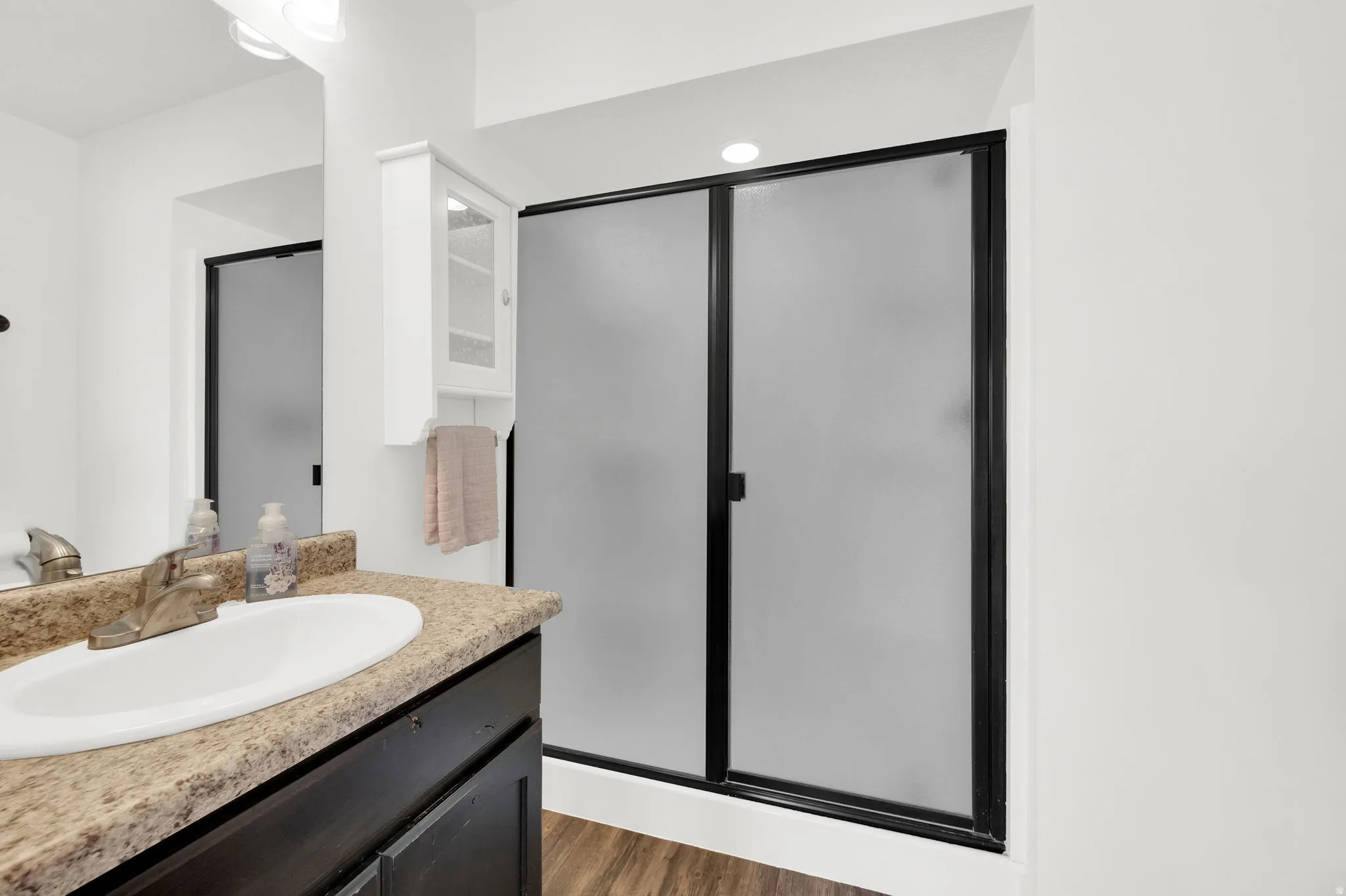 Bathroom featuring a dark wood-finish vanity with an integrated sink and light-toned countertop, a large mirror, and overhead vanity lighting