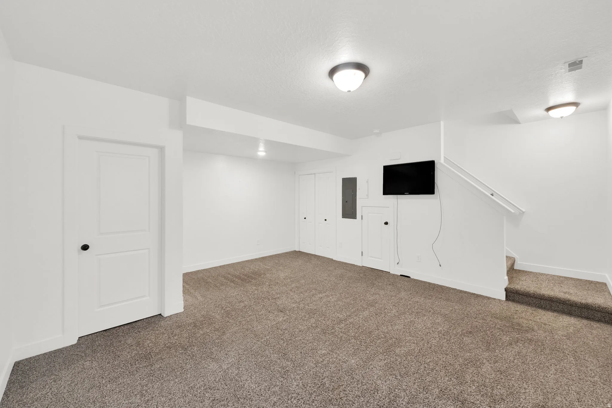 Expansive carpeted area featuring neutral-toned walls, white trim, and two-panel interior doors with matte black hardware